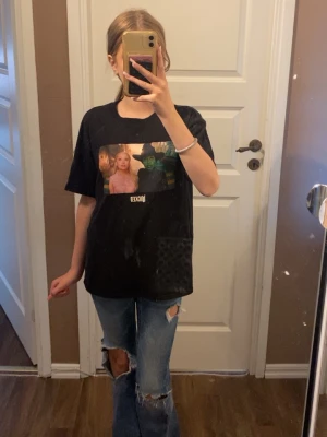 Svart oversized t-shirt med tryck - Cool svart oversized t-shirt med färgglatt tryck från musikalen Wicked på bröstet. T-shirten har rund hals och korta ärmar, perfekt för en avslappnad och trendig look. Passar dig som gillar statement-plagg och popkultur. Storlek S