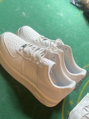 Nike airforce  - Snygga helvita sneakers med låg profil och perforerad tå för extra ventilation. Skorna har en stilren design med matchande vita skosnören och sula. Tillverkade i läder med detaljer i samma färg för en clean look.