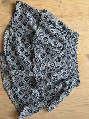 Blåmönstrad kortkjol med volang - Supersöt kortkjol med blått och vitt mönster, elastisk midja och volangkant. Perfekt för dig som gillar boho-stil och vill ha något luftigt och bekvämt. Kjolen har ett unikt tryck och passar perfekt till sommaren.