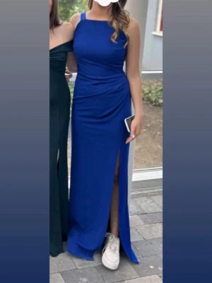 Blå lång bal klänning  med slits - Snygg blå långklänning med smala axelband och figurnära passform. Klänningen har en hög slits på ena sidan och en stilren, öppen rygg. Perfekt för bal eller student. Materialet känns mjukt och följsamt, troligtvis polyester eller liknande.