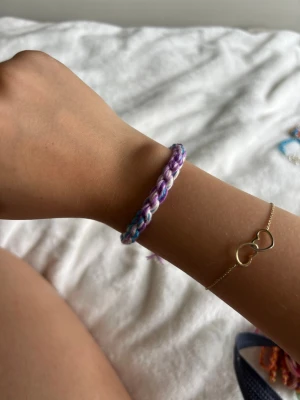 Färgglatt flätat vänskapsarmband - Ett handgjort vänskapsarmband i flätad design med lila, blå och vita toner. Armbandet är gjort av mjukt garn och dra i tofsar i ändarna för justerbar passform. Perfekt för att ge en personlig touch till din stil.💕