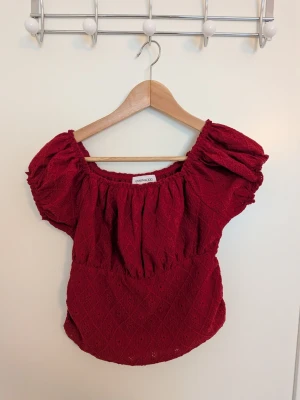 Röd offshoulder topp - Säljer en röd offshoulder topp med puffiga korta ärmar och smockad resår vid halsringningen. Toppen har ett diskret strukturmönster och är perfekt för dig som vill ha en trendig och bekväm look. Materialet känns mjukt och luftigt.