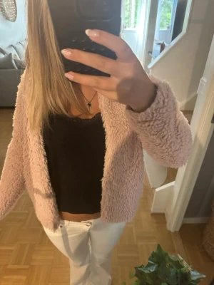 Ljusrosa teddyjacka i fluffigt material - Supersöt ljusrosa teddyjacka med fluffig och mjuk känsla. Jackan har öppen front utan synliga knappar eller dragkedja och är midjekort i modellen. Perfekt för dig som vill ha en mysig och trendig look till hösten eller vintern.