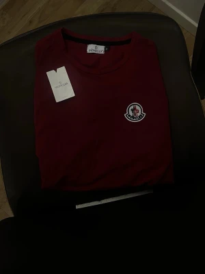 Vinröd Moncler t-shirt med logga - Snygg vinröd t-shirt från Moncler med klassisk logga på bröstet. T-shirten har rund hals och korta ärmar, perfekt för en clean och stilren look. Skriv vid funderingar 