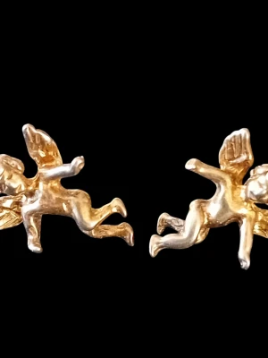 Skultuna ängelörhängen i guldpläterad sterling silver - Säljer ett par örhängen i form av änglar. De har detaljerade vingar och en lekfull design som sticker ut. Perfekta för dig som gillar unika och söta accessoarer. Äldre modellen (ej den som säljs nu).  Det ena låset till örhängena har mörknat något. Båda låsen är stämplade med SGP 925. 