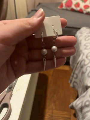 Silvriga örhängen med pärldetalj - Säljer ett par snygga hängande örhängen i silverfärg med vita pärlor och spetsiga metallhängen. Örhängena har en modern och edgy look som passar perfekt till dig som vill sticka ut lite extra.