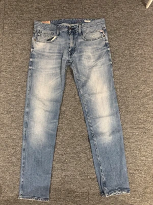 Replay Anbass Ljusblå raka jeans med slitningar - Säljer ett par ljusblå jeans med raka ben och snygga slitningar på fickorna och låren. Jeansen har klassisk femficksdesign och är gjorda i denim med en tvättad look. Perfekta för en avslappnad och trendig stil. Är 175 och väger 65 och de är för stora. Dom passar som vanliga 32, 32