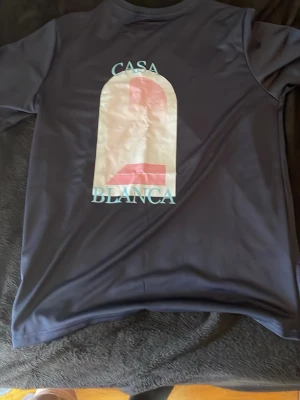 Mörkblå Casa Blanca t-shirt - Snygg mörkblå t-shirt med tryck från Casa Blanca på både bröstet och ryggen. T-shirten har rund hals och korta ärmar. Materialet känns mjukt och följsamt, perfekt för en avslappnad stil.