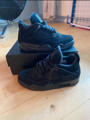 Jorden 4 black cat - Snygga helsvarta sneakers med en mix av mocka och meshdetaljer. Skorna har en chunky sula, synliga luftbubblor och coola plastdetaljer vid snörningen. Perfekta för dig som gillar en clean och sportig look.