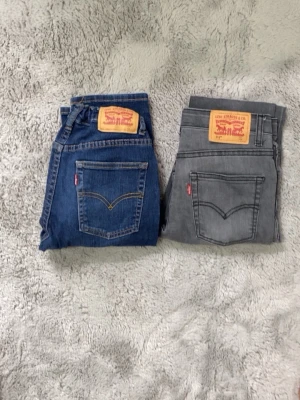 Levi's blå raka jeans samt grå jeans  (152 ) - Säljer ett par klassiska blå jeans från Levi's med raka ben och femficksmodell. Jeansen har en snygg mörkblå tvätt, kontrastsömmar och den ikoniska läderpatchen bak i midjan. Perfekta för en avslappnad och trendig look.