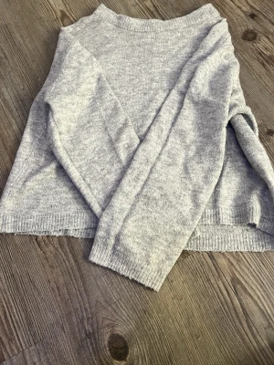Ljusgrå stickad tröja - En enkel och stilren ljusgrå stickad tröja med rund halsringning och långa ärmar. Tröjan har ribbade muddar vid ärmslut och nederkant. Perfekt för lager på lager och passar till det mesta.