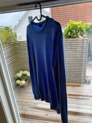 Blå tunnstickad tröja rund hals - Snygg blå tunnstickad tröja med rund halsringning och långa ärmar. Tröjan har ribbade muddar vid ärmslut och nederkant, vilket ger en clean och stilren look. Perfekt att slänga på sig över en t-shirt eller bära som den är.