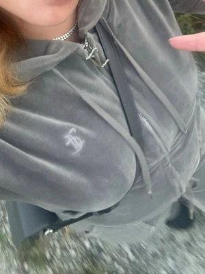 Grå velourhoodie Juicy Couture - Grå velourhoodie från Juicy Couture med dragkedja, huva och snörning. Tröjan har broderad logga på bröstet och praktiska fickor framtill. Perfekt för en chill och trendig stil! Inga större tecken på användning!🌷 Matchande Byxor finns också till salu i min profil!🌷 Vid köp av både Hoodien & Matchande Byxor kan det bli billigare än att köpa separat!🤩 