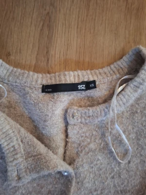 Beige stickad tröja från lager 157 - Mysig beige stickad tröja från lager 157 i storlek XS. Tröjan har korta ärmar, rund halsringning och ribbstickade detaljer vid hals och nederkant. Perfekt för lager på lager och enkel att matcha med olika outfits. Vissa knappar har åkt av!