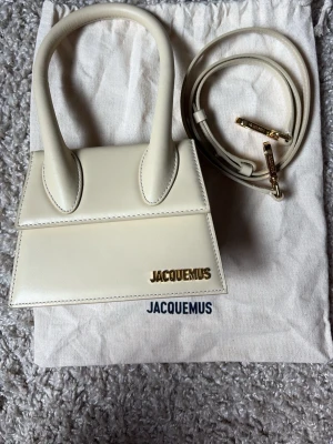 Jacquemus Le Chiquito Moyen - Jacquemus Le Chiquito Moyen i en elegant beige färg. Väskan är helt oanvänd och i nyskick, då den endast har förvarats i sin dustbag. Originalremmen med guldfärgade detaljer är också helt oanvänd och medföljer, liksom original dustbag. Tillverkad i 100 % läder. Väskan var en present men kom aldrig till användning då modellen inte passade min stil. NYPRIS: 9200