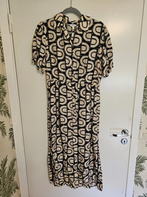 Midiklänning Objada  - Beige och blåmönstrad midiklänning långklänning från Object. Klänningen har korta puffärmar, krage och knappar framtill. 