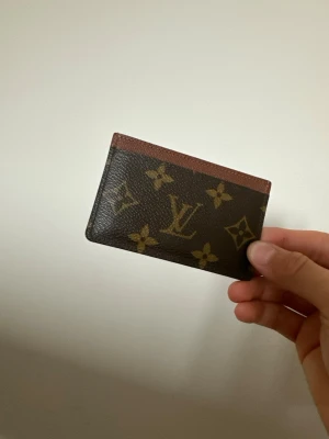 Louis Vuitton Plånbok - Snygg korthållare från Louis Vuitton i klassiskt brunt monogrammönster med beige och guldiga detaljer. Tillverkad i tåligt läder med en stilren och smidig design som passar perfekt i fickan. Perfekt för dig som vill ha en lyxig accessoar.