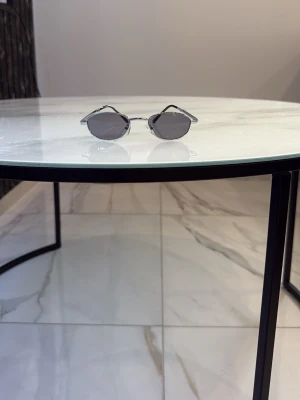 Silvriga ovala solglasögon - Snygga solglasögon med tunn, silvrig metallbåge och ovala, mörktonade glas. Minimalistisk och trendig design som passar perfekt till sommarens alla outfits. Lätta att matcha och ger en cool vibe.