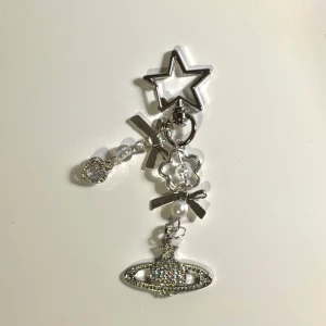 Silvrig smyckesberlock med rosett och stjärna - Snygg silvrig smyckesberlock med stjärnformad clip, glittrande planetmotiv, pärldetaljer och en liten blomma 𓂃˖ ࣪⊹ Perfekt att hänga på väskan som nyckelknippa eller som dekoration till rummet. Ger en cool och unik touch till din stil!