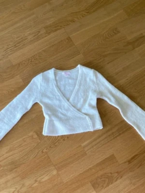 Vit omlottkofta från Gina Tricot - Säljer en vit stickad omlottkofta från Gina Tricot. Koftan har långa ärmar, v-ringning och knäppning i sidan. Perfekt att slänga över en topp för en chill och trendig look.