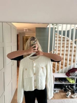 Vit bouclékofta med guldknappar - Säljer en superfin vit bouclékofta med dekorativa guldknappar och två bröstfickor. Koftan har rund halsringning, lång ärm och en lyxig struktur som ger en trendig look. Perfekt att styla till jeans eller kjol för en chic vibe.