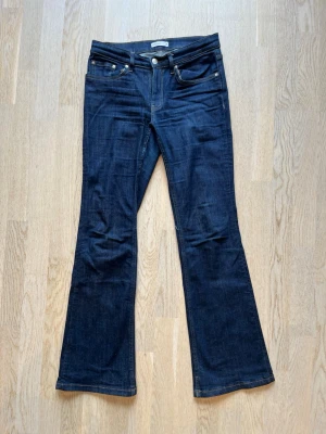 Mörkblå bootcut jeans - Snygga mörkblå jeans med bootcut passform och klassisk femficksdesign. Jeansen har låg midja och är tillverkade i ett mjukt denimtyg som ger en skön känsla. Perfekta för dig som gillar en tidlös och avslappnad stil. Köpt secondhand med prislapp kvar, använd 2-3 gånger. Deffekt vid gylfen har lagats. Tveka inte på att skriva en fråga eller be om fler bilder.🌸🌸