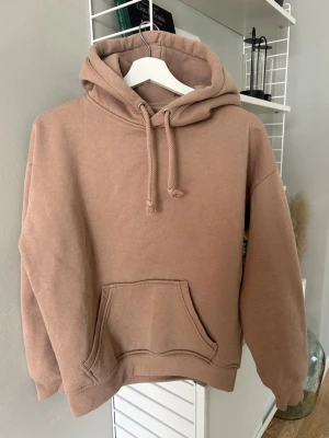 Beige oversized hoodie med huva - En stilren beige hoodie i oversized modell med stor ficka framtill. Tillverkad i mjukt bomullsmaterial och har ribbade muddar vid ärmslut och nederkant. Perfekt för en avslappnad och trendig look.