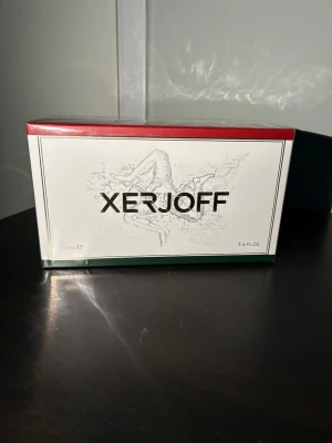 Xerjoff Naxos Eau de Parfum - Lyxig parfym från Xerjoff i modellen Naxos. Förpackningen är elegant med vit framsida, röda och gröna detaljer samt Xerjoff-loggan i svart. Kartongen har en konstnärlig illustration och rymmer 100 ml (3.4 fl oz) Eau de Parfum.