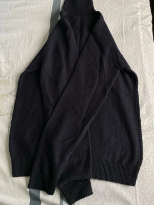 Svart stickad polotröja - Mysig svart stickad polotröja med långa ärmar och ribbade muddar vid ärmslut och nederkant. Perfekt för lager på lager och enkel att matcha med olika outfits.