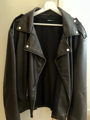 Svart skinnjacka från Gina Tricot - Snygg brun  skinnjacka från Gina Tricot med klassisk bikerstil, breda slag och silverfärgade detaljer. Jackan har dragkedja framtill och dekorativa knappar på kragen. Perfekt för en cool och trendig look. Storlek XL/XXL
