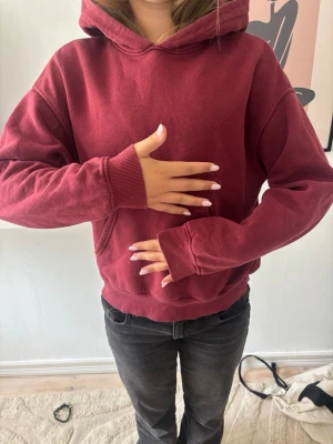 Vinröd hoodie med huva - Säljer en vinröd hoodie med huva och ribbade muddar vid ärmslut och nederkant. Hoodien har en avslappnad passform och är tillverkad i mjukt bomullsliknande material. Perfekt för dig som gillar en enkel och stilren look.