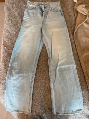Ljusblå raka jeans från Levi's - Säljer ett par ljusblå jeans från Levi's med rak passform och klassisk femficksdesign. Jeansen har hög midja och är tillverkade i slitstark denim med Levi's ikoniska läderpatch bak. Perfekta för en avslappnad och trendig look.
