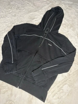 Svart Hugo boss hoodie - Säljer en svart Hugo boss hoodie i storleken M men passar även S. Hoodien är i okej skick då den har ett pyttelite hål  vid armen men som ej är synligt och går att sy om man skulle vilja. Kom gärna privat för mer information eller bilder på hoodien😊