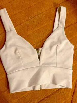 Nly Trend croppad bustiertopp med dragkedja - strl.XS - Snygg vit croppad linnetopp med breda axelband och markerad midja. Toppen har en djup v-ringning och dragkedja bak för en edgy look. Perfekt att styla med höga jeans eller kjol för en trendig outfit. Helt ny med tags kvar! Strl.XS (stretchig)