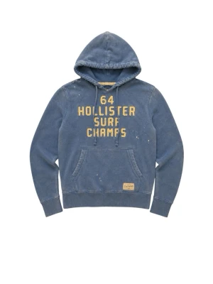 Blå hoodie Hollister Surf Champs - Blå hoodie från Hollister med gul text '64 Hollister Surf Champs' på bröstet. Klassisk känguruficka framtill och huva med dragsko. Hoodien har en tvättad vintage-look och detaljer i form av små vita färgstänk. Perfekt för en avslappnad streetwear-stil.