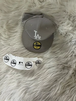 Grå LA 59FIFTY keps - Snygg grå 59FIFTY keps från New Era med LA-logga broderad framtill och MLB-logga bak. Klassisk rak skärm och klistermärke kvar på skärmen. Tillverkad i bomullsmix, perfekt för dig som gillar streetwear och sportig stil.