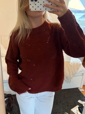 Mörkröd stickad tröja - Mysig mörkröd stickad tröja med rund halsringning och långa ärmar. Tröjan har en avslappnad passform och är tillverkad i ett mjukt, grovt stickat material. Perfekt för kyligare dagar och enkel att styla med jeans eller kjol.