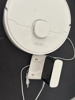 Vit robotdammsugare Dreame - Dreame robotdammsugare med laddstation. Visar felmeddelandet ‘Please check if the dispensing cover is jammed’. Har kontrollerat att luckan inte sitter fast, men felet kvarstår. Säljs därför som reparationsobjekt. Pris kan diskuteras men då jag har köpt den för ca 2000kr så säljer jag den för 600. (Pris kan diskuteras. Säljer en vit robotdammsugare från Dreame med laddstation. Den har rund form, borsthuvud undertill och flera knappar på ovansidan. 