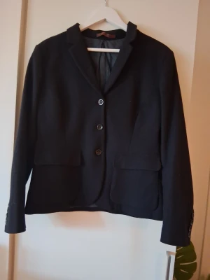 Svart klassisk kavaj med fickor Peak Performance L - Stilren svart kavaj med tre knappar framtill och två stora fickor. Kavajen har smal krage och knappar även vid ärmsluten. Passar perfekt till en dressad look och är tillverkad i ett mjukt tyg som ger en snygg siluett.