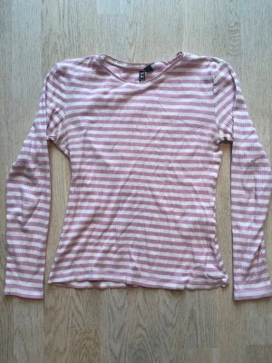 Rosa och vit randig långärmad topp - Säljer en långärmad topp från Pieces i mjuk bomull. Toppen har ett randigt mönster i ljusrosa och vitt, rund halsringning och en slim passform. Perfekt för dig som gillar en enkel men söt stil. Tveka inte på att skriva en fråga eller be om fler bilder.🌸🌸