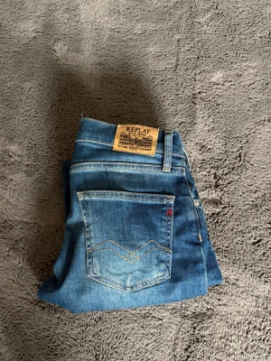 Blå jeans från Replay - Snygga blå jeans från Replay med klassisk femficksmodell och ljusa slitningar framtill. Jeansen har normal midja, bälteshällor och en patch med Replay-logga bak i midjan. Perfekta för en avslappnad och trendig look.