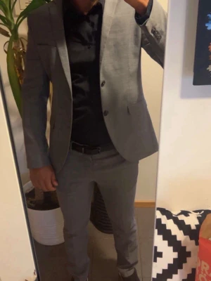 Grå kostym  - Säljer en stilren grå kostym med matchande kavaj och byxor. Kavajen har två knappar, klassisk krage och fickor framtill. Passar perfekt till en svart skjorta för en clean och modern look. Endast använd ett fåtal gånger så den är i fint skick! Säljer pga att den blivit för liten. Ny pris ca 1600kr. Pris kan diskuteras vid snabb affär 