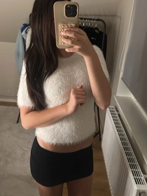 Vit fluffig croppad topp - Säljer en supermjuk och fluffig vit croppad topp med korta ärmar. Toppen har en rund halsringning och är perfekt för dig som vill ha en mysig men ändå stylish look. Materialet känns lent och ger en cool textur till outfiten.