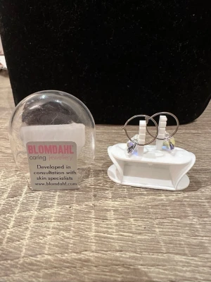 Blomdahl örhängen med hjärthänge - Säljer ett par stilrena örhängen från Blomdahl med silverfärgade ringar och gnistrande hjärtformade hängen i transparent kristall. Perfekta för dig som gillar diskret men ändå unik design. Kommer i originalförpackning.