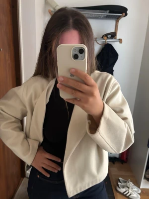 Beige omlottjacka i ullmix - Snygg beige omlottjacka med minimalistisk design och rak passform. Jackan har lång ärm och är tillverkad i en mjuk ullblandning som passar perfekt till både jeans och kjol. Enkel att styla och ger en clean look.
