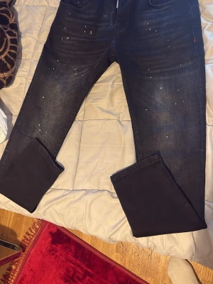 Mörkblå slim fit jeans med stänk - Snygga mörkblå jeans i slim fit-modell med vita färgstänk som ger en trendig och avslappnad look. Jeansen har klassisk femficksdesign och är tillverkade i ett stretchigt denimtyg för extra komfort. Perfekta för dig som gillar streetwear och vill sticka ut.