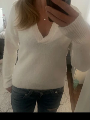 Vit stickad tröja från Reserved - Säljer en stilren vit stickad tröja från Reserved i storlek S. Tröjan har djup v-ringning, långa ärmar och ribbade muddar vid ärmslut och nederkant. Perfekt att matcha med jeans för en enkel och snygg look. Krämvit
