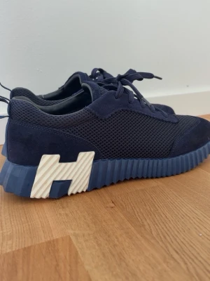 H Skor - Snygga mörkblå sneakers med ovandel i mesh och mocka, samt en unik detalj med en vit H-formad dekoration på sulan. Box finns om man vill!