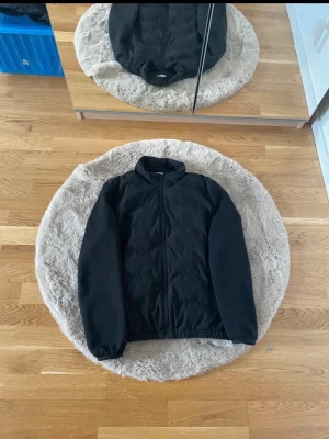 Svart Zara cardigan med dragkedja - Svart Zara cardigan med dragkedja framtill och elastiska muddar vid ärmslut och midja. Jackan har en enkel, stilren design och står emot vind bra. Perfekt för dig som vill ha en lätt och smidig jacka till vardags.