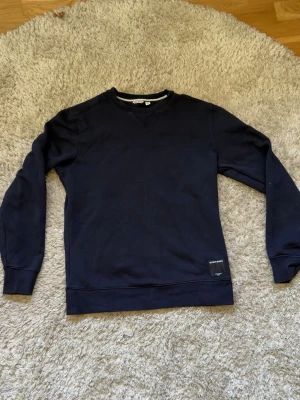 Mörkblå sweatshirt från Björn Borg - Klassisk mörkblå sweatshirt från Björn Borg med rund halsringning och ribbade muddar vid ärmslut och nederkant. Tröjan har en diskret patch med logga nertill och är tillverkad i mjuk bomullsblandning. Perfekt för en avslappnad och stilren look.
